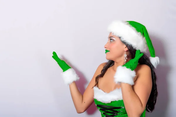 一个年轻美丽的黑发姑娘 穿着绿色的圣诞老人礼服 带着惊讶的表情暗示着什么 — 图库照片