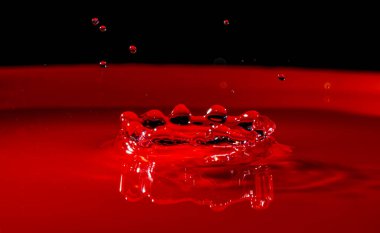 Su kaplaması, siyah arka planı olan kırmızı bir kabın içinde makro modda çekilmiş dairesel bir sıçrama ile oluşmuştur..