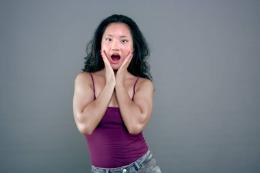 Asyalı etnik Asyalı kadının elleri yüzlerinde ve şaşkınlık ifadesi ile çekilmiş bir fotoğrafı.