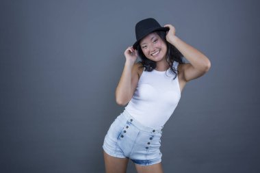 Young ethnic Asian woman posing in tank top, shorts and hat.