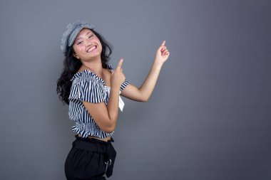 smiling young woman of Asian ethnicity pointing to her isolate in the background