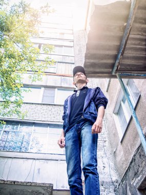 Şapkalı ve kapüşonlu genç bir adam çok katlı bir binanın arka planına bakıyor.