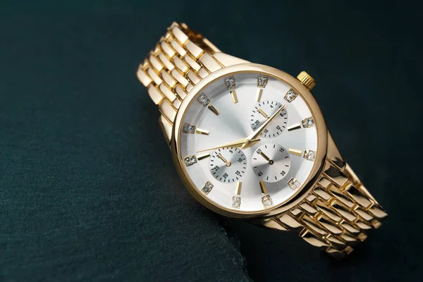Eine goldene Armbanduhr mit weißem Zifferblatt ruht auf einem Steintisch. Stockfoto