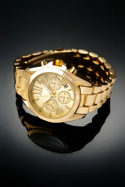 Reloj de pulsera de oro con esfera dorada se encuentra en una superficie reflectante brillante negro — Foto de Stock