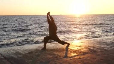 Sakallı adam gün doğumunda yoga yapıyor. 