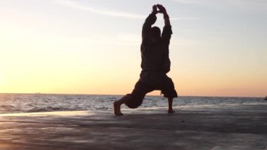 Sakallı adam gün doğumunda yoga yapıyor. 