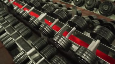 Mavi tişörtlü bir adam spor salonunda dambıl kaldırıyor.