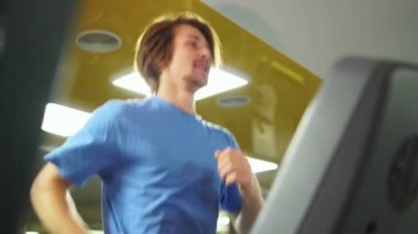 Spor salonunda koşu bandı. Mavi tişörtlü adam.