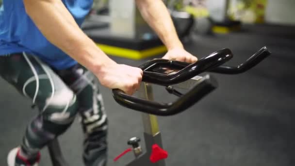 En rödhårig kille i blå t-shirt cyklar på gymmet. närbild av en hand — Stockvideo