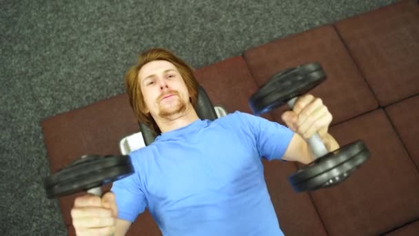 Anak muda mengangkat dumbbells sementara lying.man dalam t-shirt biru adalah kenaikan di gym — Stok Video