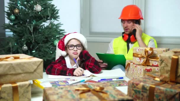 Menina desenha no fundo da árvore de Natal.engineer com sua filha — Vídeo de Stock