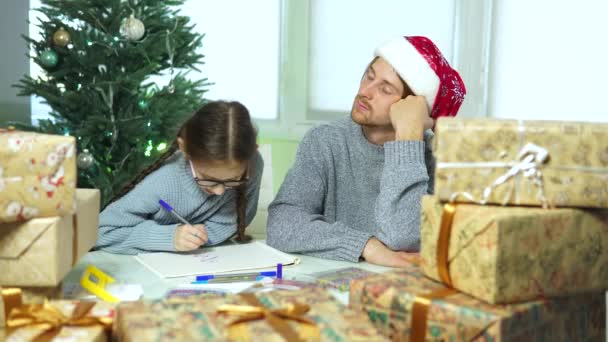 Pai e filha no Natal. Menina desenha com um homem de chapéu de Pai Natal — Vídeo de Stock
