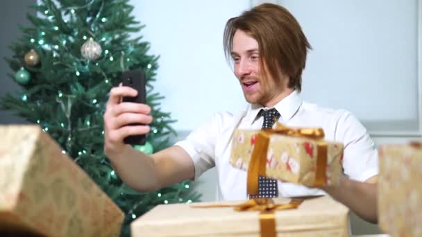 Młody biznesmen rozmawia z kamerą siedzi w office.shows prezentów noworocznych — Wideo stockowe