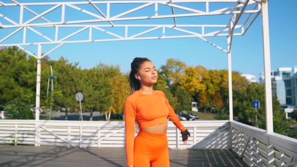Chica de piel oscura en un traje naranja se tira contra un cielo azul y el mar — Vídeos de Stock