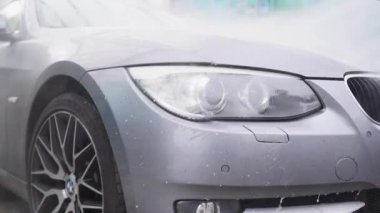 Gri bir arabayı kapat. Arabanın farını yüksek basınçlı suyla yıka.