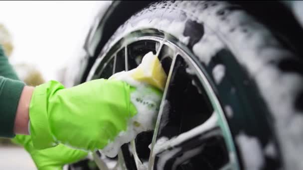 Homem em luvas verdes esfrega carro tire.washes jantes de carro com espuma com esponja amarela — Vídeo de Stock