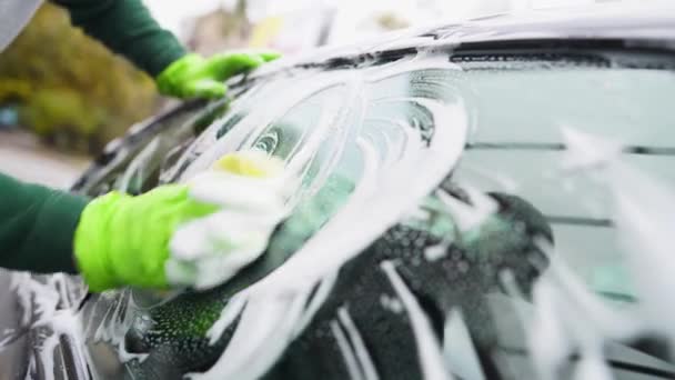 Крупним планом. молодий хлопець миє свою машину. натирає бокове скло сірого автомобіля — стокове відео