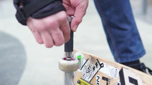 Close-up de como as mãos torcem uma roda colorida de uma prancha de skate em adesivos — Vídeo de Stock