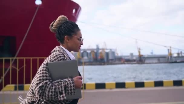 Wanita berkulit gelap berkacamata berjalan dengan kapal besar di latar belakang — Stok Video