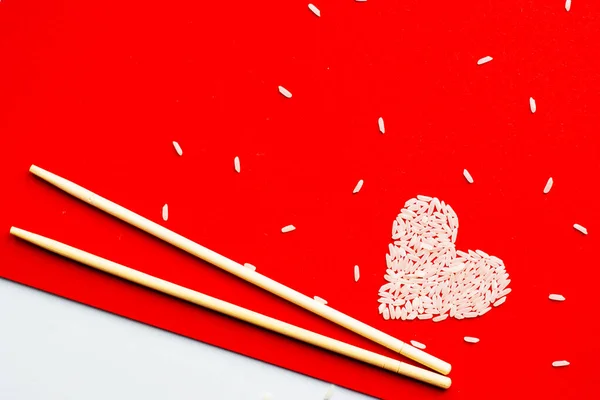 Kırmızı zemin üzerinde pirinçten yapılmış bir kalp. Suşi çubukları
