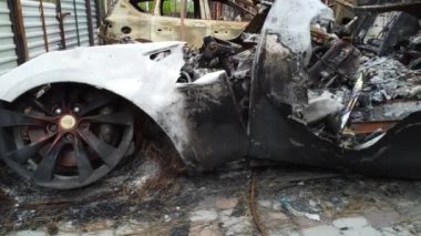 HOSTOMEL, UKRAINE, 26 Mayıs 2022. Evin bahçesinde yanan Tesla aracı. Ukrayna 'da savaş. Şehrin bombalanmış yerleşim bölgesi. Bombardımandan sonra ev cephesi. Bir evin yıkıntıları. İnşa kalıntıları. 