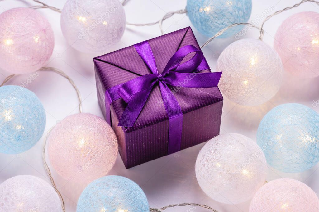 Gift in a shiny purple box and glowing Christmas balls. Festive mood, christmas concept.