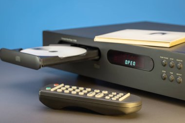 CD çalar, disk tepsisini aç, masadaki uzaktan kumanda. Yakın plan, mavi arkaplan.