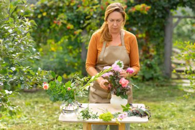 Orta yaşlı bir çiçekçi kadın bahçesinde bir buket yapıyor. Orta yaşlı serbest çalışan..