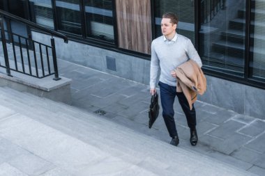 Yorgun ofis çalışanı merdivenlerden çıkar, bir elinde palto, diğer elinde iş çantası vardır. Çalışma gününün sonu.