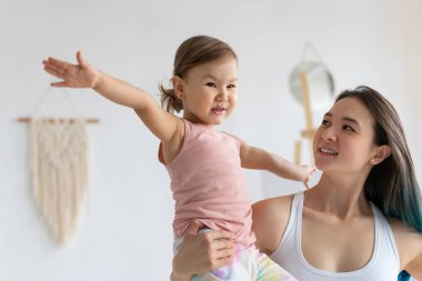 Küçük kızı olan genç bir anne yoga evinde pratik yapıyor. Savaşçı pozu.