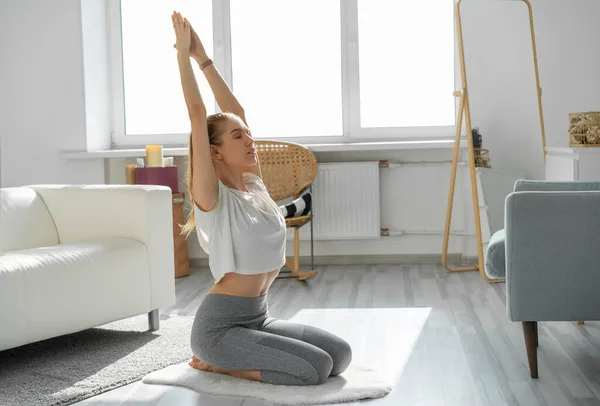 Evde yün halıda yoga yapan genç bir kadın..