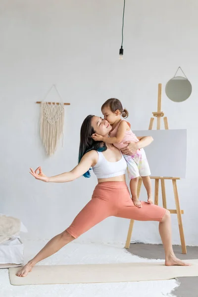 Little daughter helps mom practice yoga. Happy and healthy family.