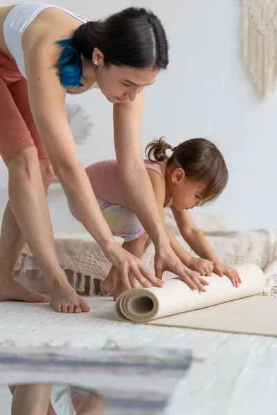 幼い娘を持つ若い母親がヨガマットを転がしています ヨガホーム — ストック写真