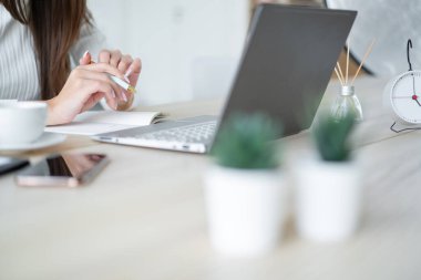 Sorunlu kazaklı genç bir kadın dizüstü bilgisayarın önünde oturuyor ve çalışma kitabına yazıyor..