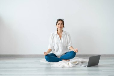 Genç kadın dizüstü bilgisayarın önünde oturuyor. Lotus pozisyonunda. Evinin zemininde, parlak odada..
