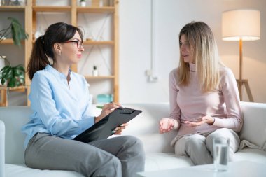 Psikolog genç bayanı dikkatle dinler ve kanepede otururken panoya yazar..