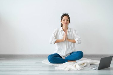 Genç kadın dizüstü bilgisayarın önünde oturuyor. Lotus pozisyonunda. Evinin zemininde, parlak odada..