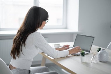 İş kadını pencerenin yanındaki masada oturuyor ve dizüstü bilgisayarda yazıyor..