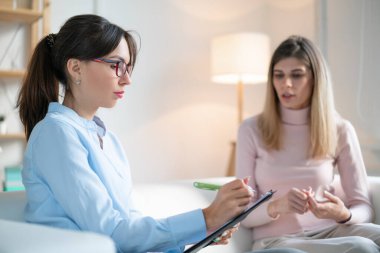 Psikolog genç bayanı dikkatle dinler ve kanepede otururken panoya yazar..