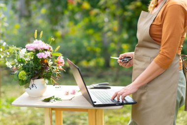 Orta yaşlı kadın çiçekçi çiçek buketlerinin üretimi ve teslimi için online siparişleri kabul ediyor. Uzaktan kumanda. Küçük işletme.