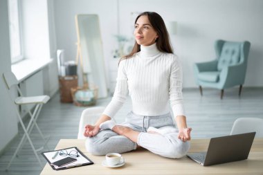 Padmasana yogasında masa başında oturan genç bir kadın ev ofisine poz veriyor..