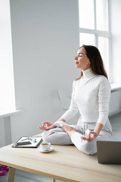 Young woman sitting on desk  in padmasana yoga pose home office.