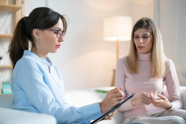 Psikolog genç bayanı dikkatle dinler ve kanepede otururken panoya yazar..