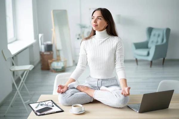 Padmasana yogasında masa başında oturan genç bir kadın ev ofisine poz veriyor..