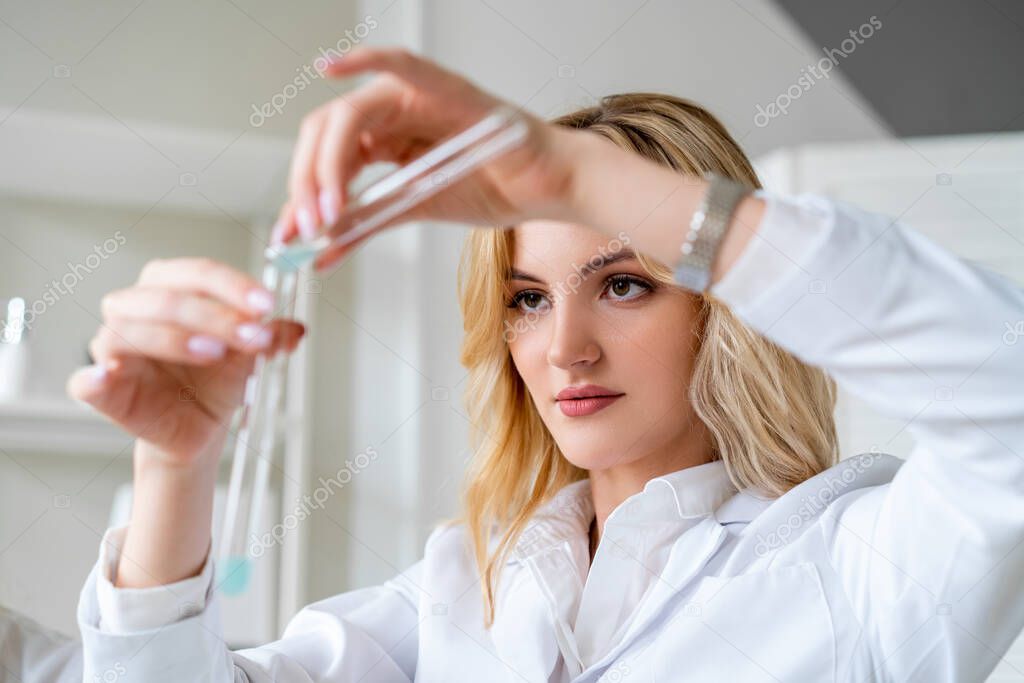 Young woman enthusiastically makes  chemical experiment, pours liquid from one test tube to another, fun work in laboratory.