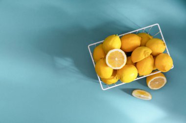 Mavi arka planda beyaz sepette taze limonlar. C vitamini konsepti, bağışıklık savunması. Üst görünüm, boşluğu kopyala.