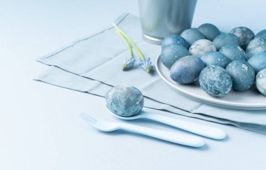 Kaşık içinde taş Paskalya yumurtası, çiçekler ve arka planda yumurta tabağı..