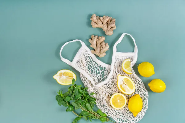 Healthy products in the form of mint, lemons and ginger roots on a string bag, on a simple light green background with copy space, the concept of an eco-friendly and healthy lifestyle.