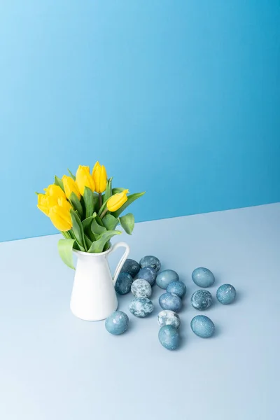 Boeket Gele Verse Tulpen Witte Kruik Geschilderde Paaseieren Blauwe Achtergrond — Stockfoto