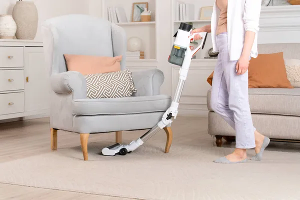 Kablosuz elektrik süpürgesiyle koltuğun altındaki halıyı temizleyen kadın. Ev temizliği.